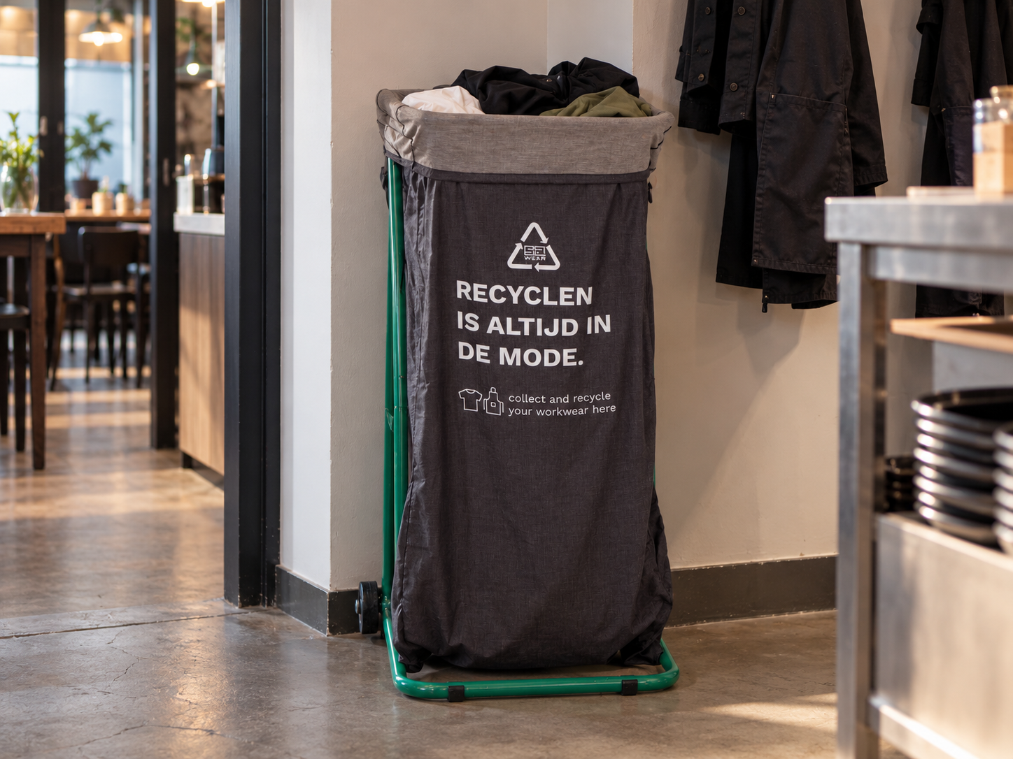 Recyclezak van SA Wear met de tekst "Recyclen is altijd in de mode" in een horecazaak, gevuld met afgedragen bedrijfskleding